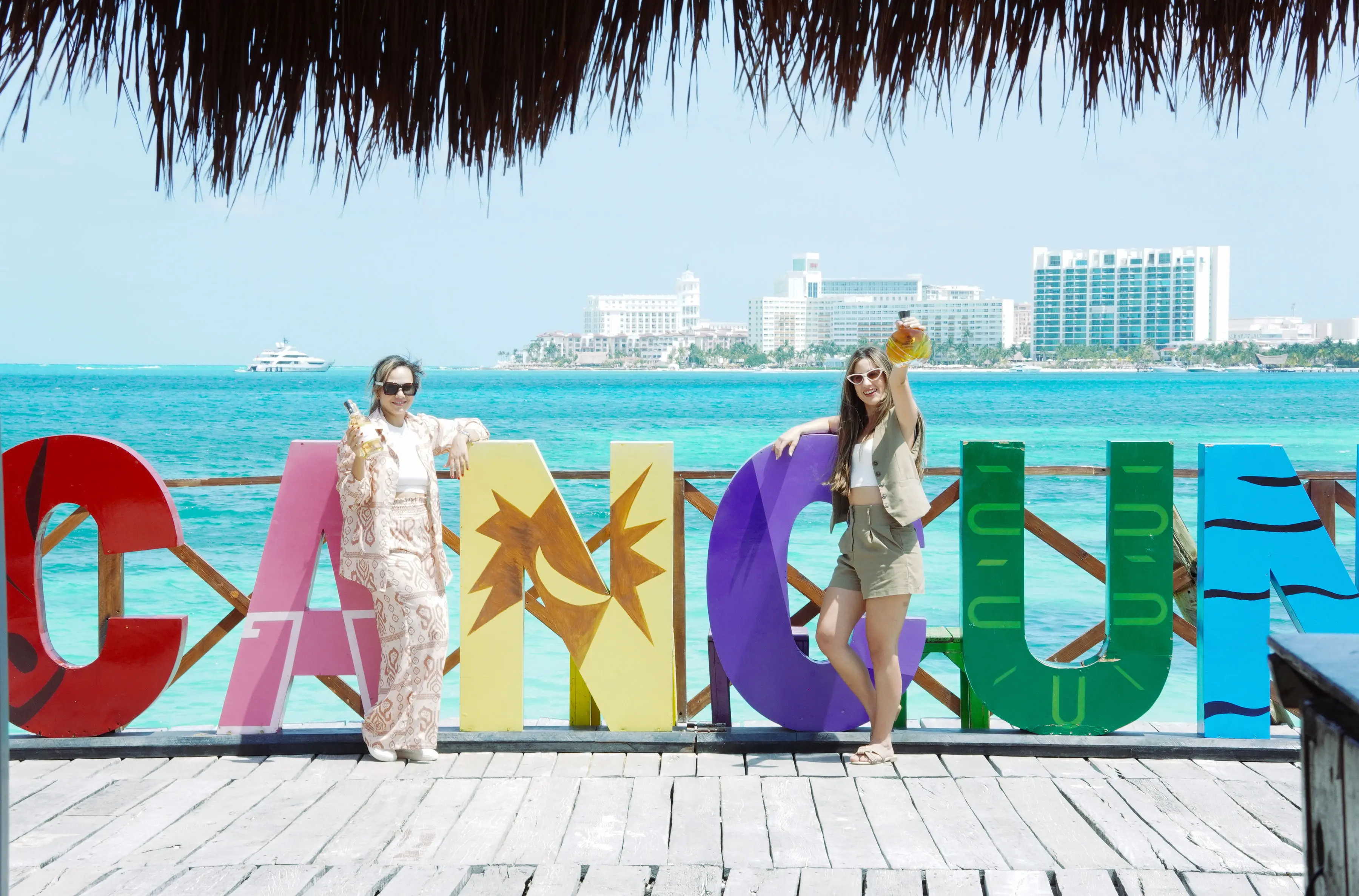 Group of friends having fun in front of the sea, posing for a photo at the Cancun sign